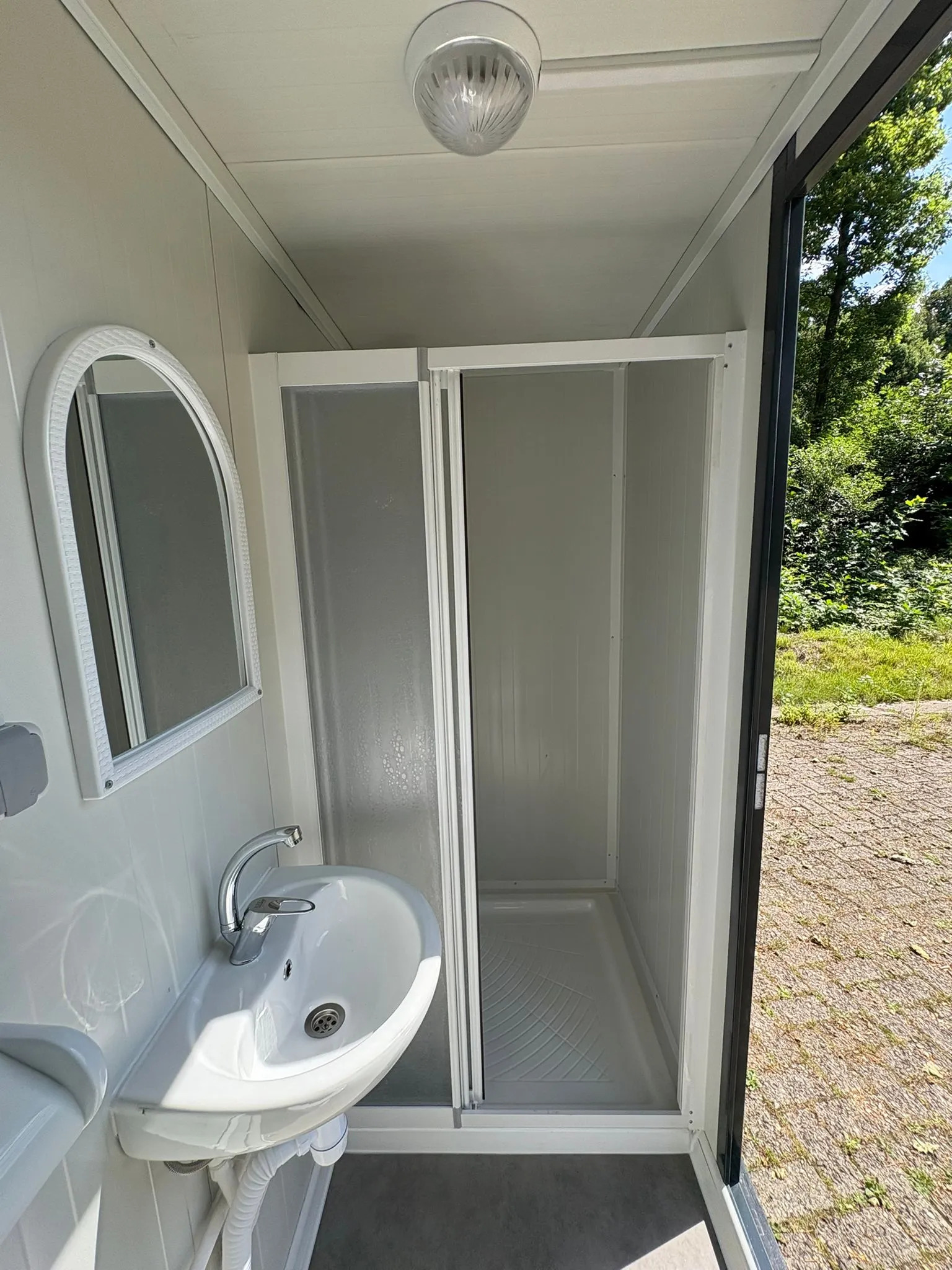 Interior of a portable bathroom unit showing shower, sink, and mirror
