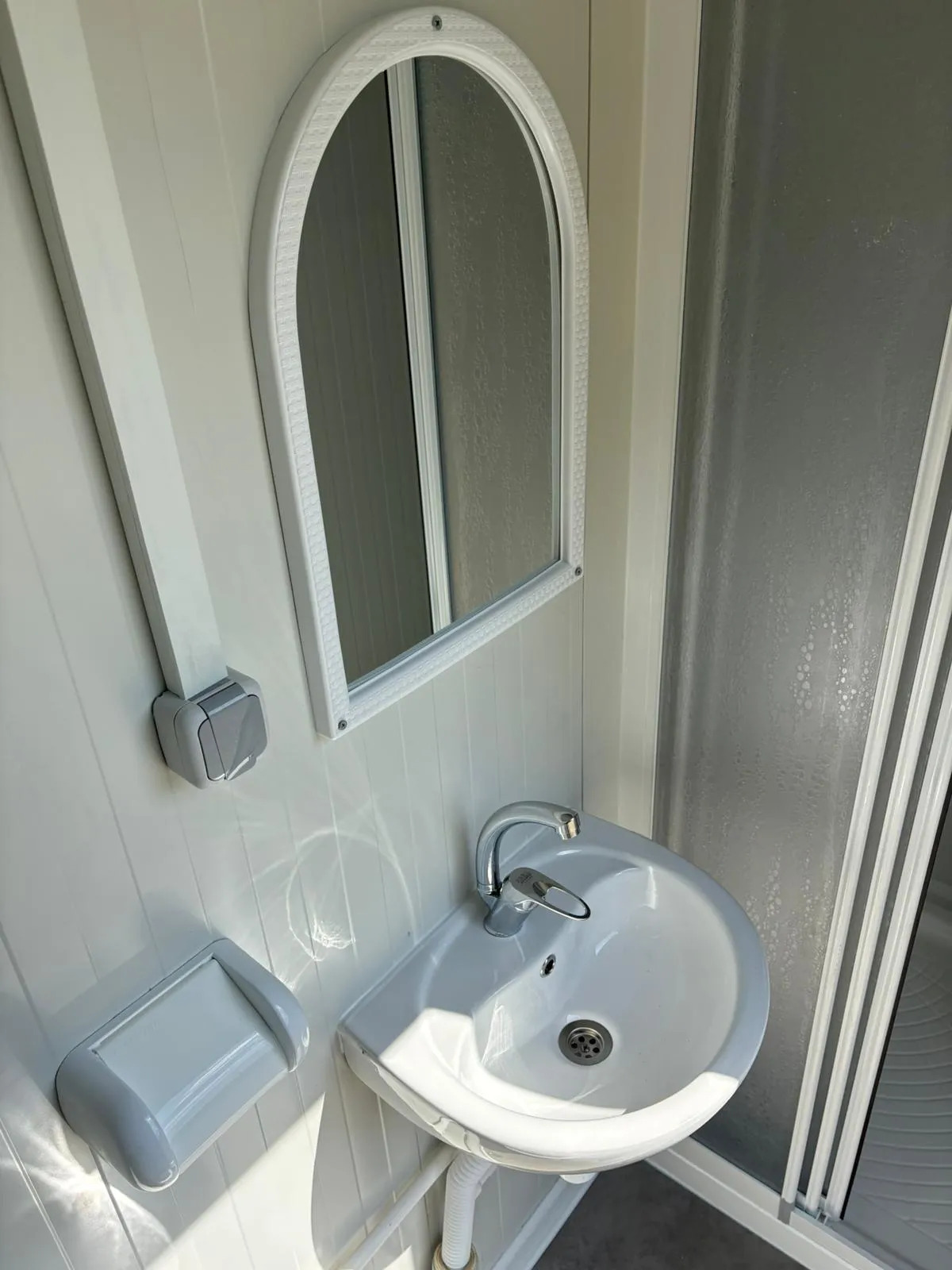 Interior of a portable bathroom unit showing sink, mirror, and toilet roll holder